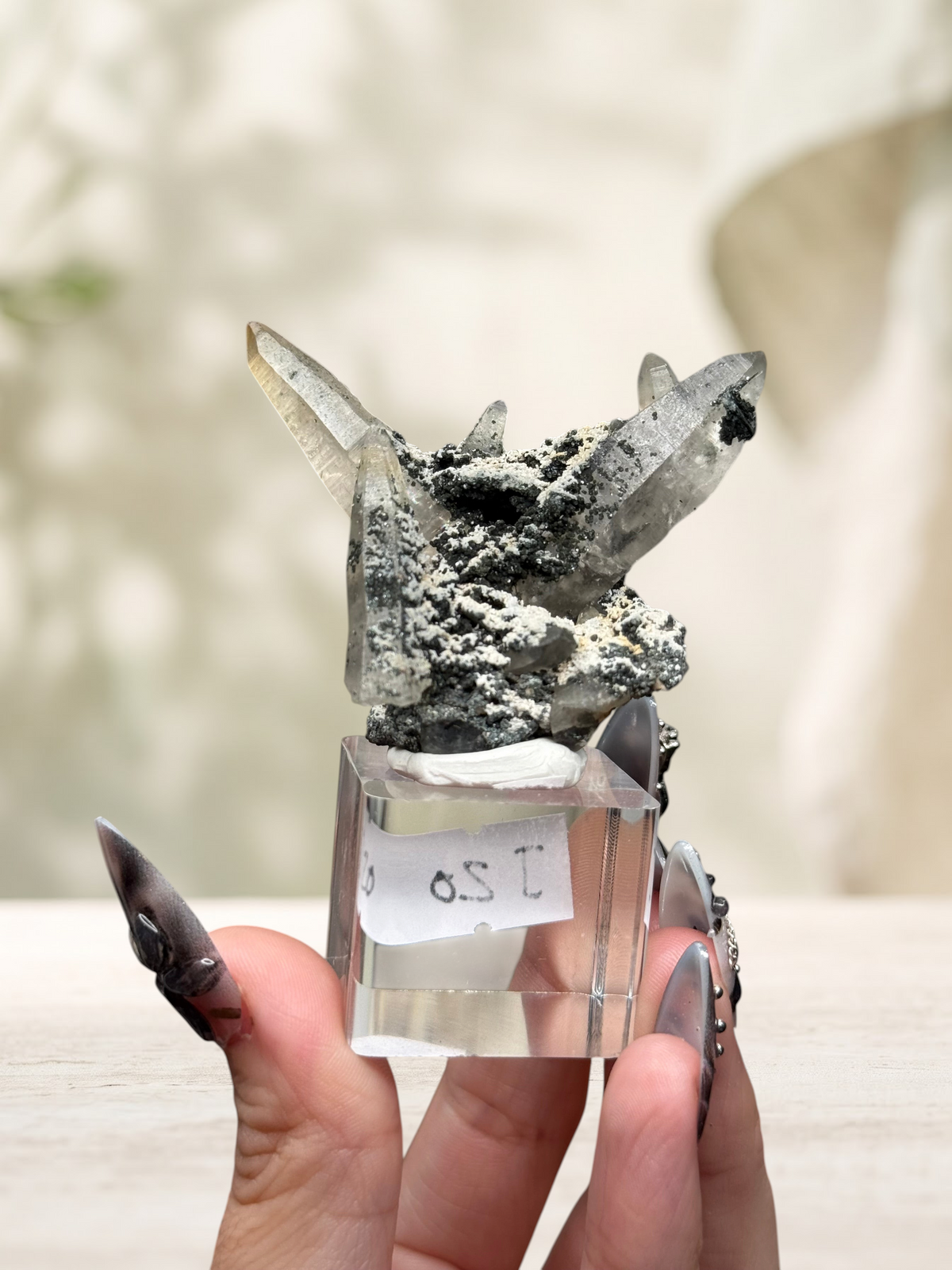 Crystal Glade laser quartz specimen from Pakistan with tapering clear crystals and dark mineral matrix on a stand