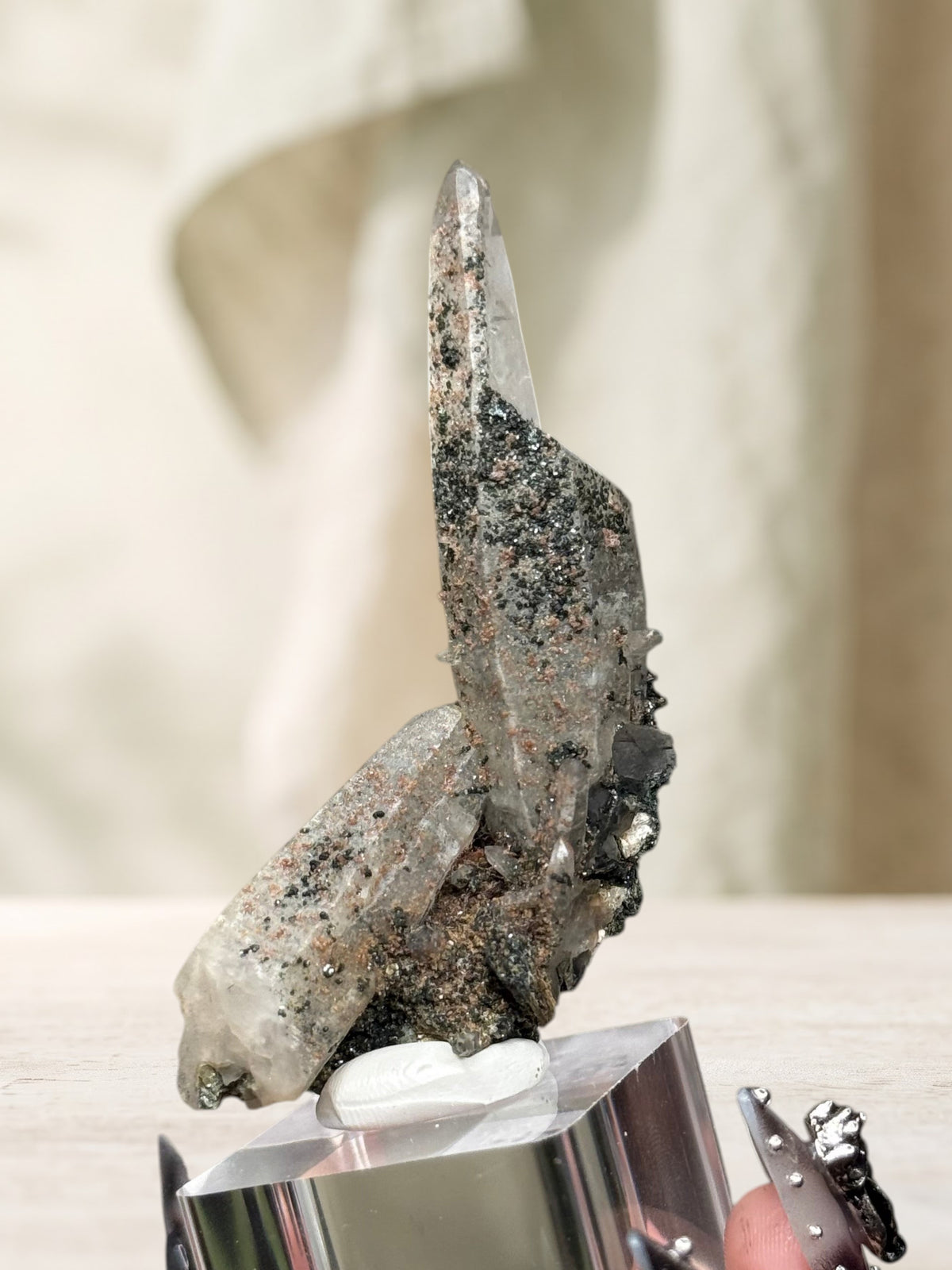 Crystal Glade laser quartz specimen from Balochistan with long tapering crystal and dark mineral inclusions on a stand