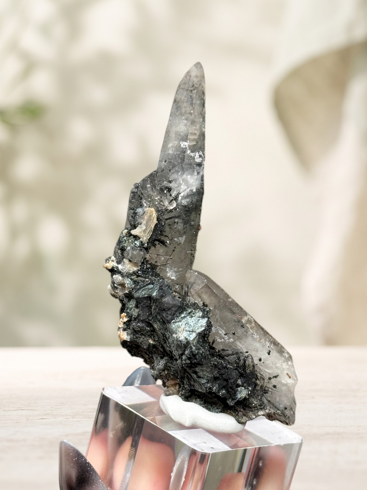 Crystal Glade natural laser quartz specimen from Pakistan with tapering point and dark mineral inclusions on a stand